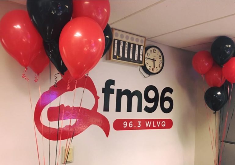FM96 radio station logo with red and black balloons and clock on wall.