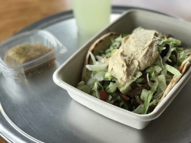 Gyro sandwich topped with hummus and lettuce in a takeout container