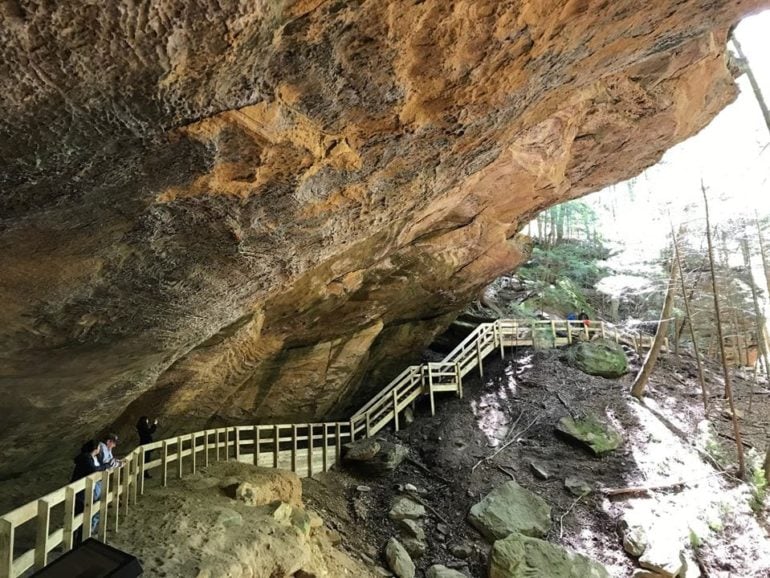 Two New Hiking Trails Opened This Week In Hocking Hills 3 Wooden boardwalk leads under large rock overhang in forested canyon area.