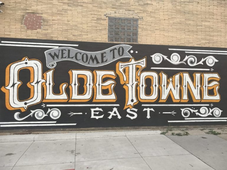 A Beginner's Guide To Gettin' Down In Olde Towne East 3 Ornate mural with "Welcome to Olde Towne East" lettering on brick building wall.