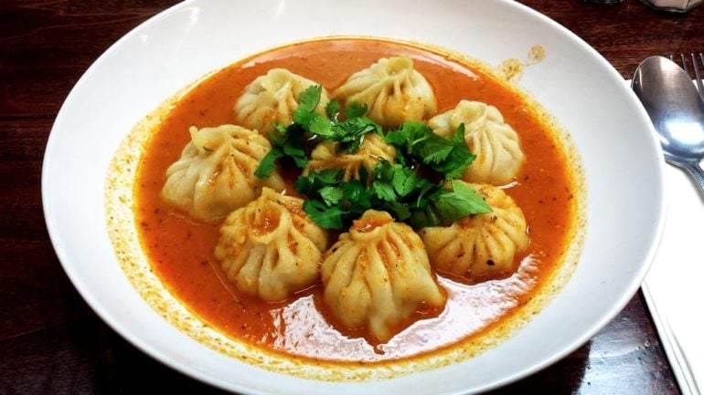 Steamed dumplings in spicy red broth garnished with fresh cilantro in white bowl.