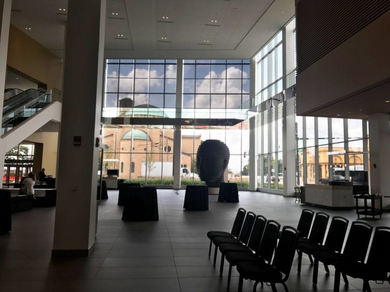 Modern interior atrium with floor-to-ceiling windows overlooking brick buildings and city streets.