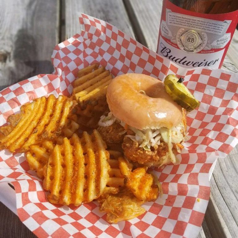 Stashed Away Behind A Bar In The Old North, Forty's Chicken & Waffles Redefines The Age Old Classic 1 Pulled pork sandwich with waffle fries, pickles, and Budweiser beer on checkered paper.