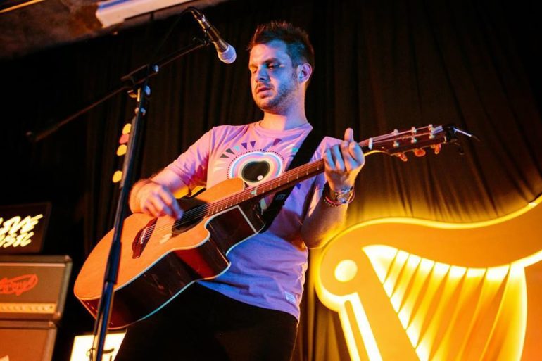 The Dopest Venues In Columbus For Intimate Shows And Cozy Concerts 2 Musician performs with acoustic guitar on stage under warm stage lighting.