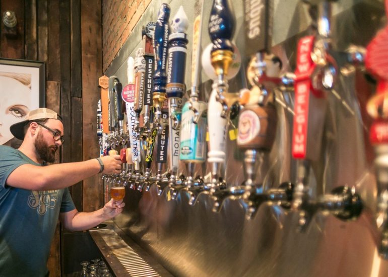 Man pouring craft beer from tap handle at brewery bar with multiple beer taps.