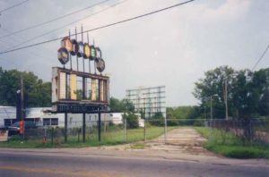Weathered marquee sign frame at the abandoned Linden Air Drive-In site with a screen visible in the distance