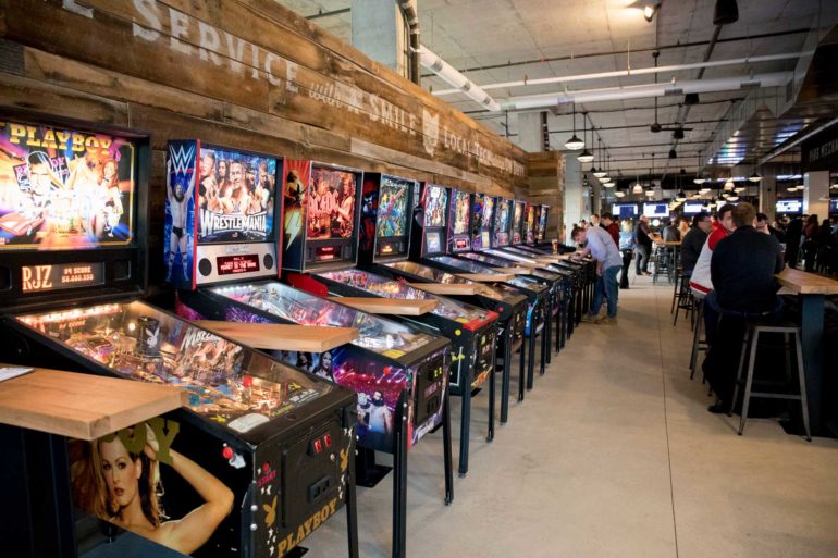 10 Things Broke 20-Somethings In Columbus Love 1 Row of pinball machines including WWE and Playboy themes along a wood-paneled wall
