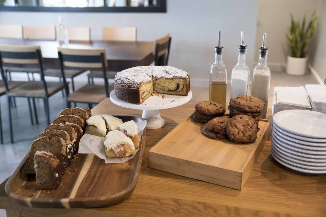 Fox In The Snow To Open Upper Arlington Location 1 Bakery display table with cake, cookies, bread, and spreads in modern café setting.