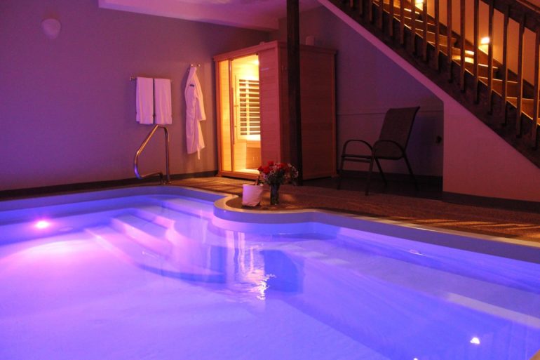 Indoor swimming pool with blue LED lighting, sauna entrance, and spa amenities at night
