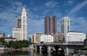 Downtown skyline featuring historic tower, modern buildings, and arched bridge over river.