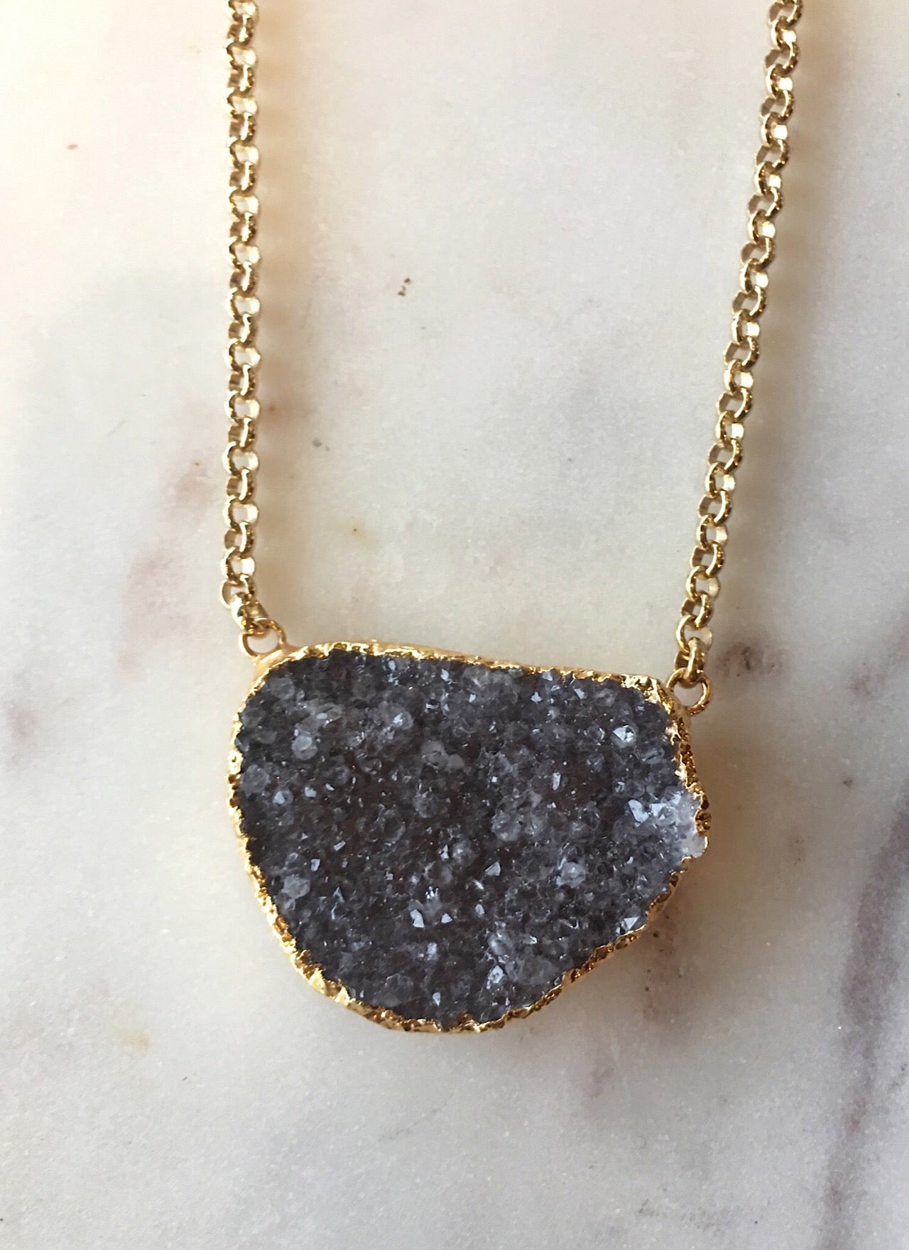 Gold necklace with a gray druzy crystal pendant on a marble surface