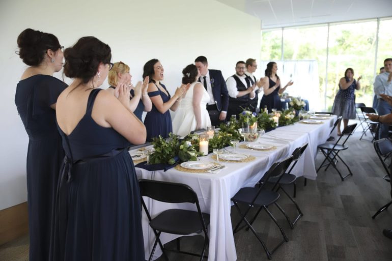 Here's What It's Like To Get Married At A Columbus Metro Park 4 Wedding reception guests stand and applaud beside a decorated dining table with white linens