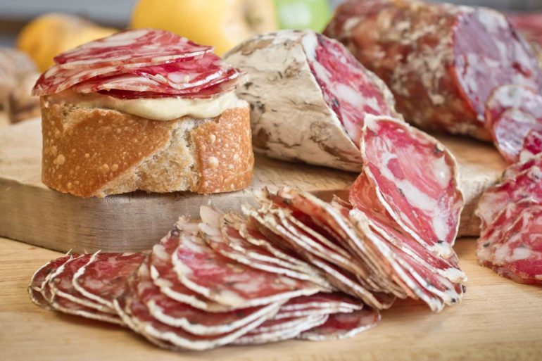 Where To Find The Best Charcuterie Boards In Columbus 1 Sliced cured salami and bread with spread on wooden cutting board.