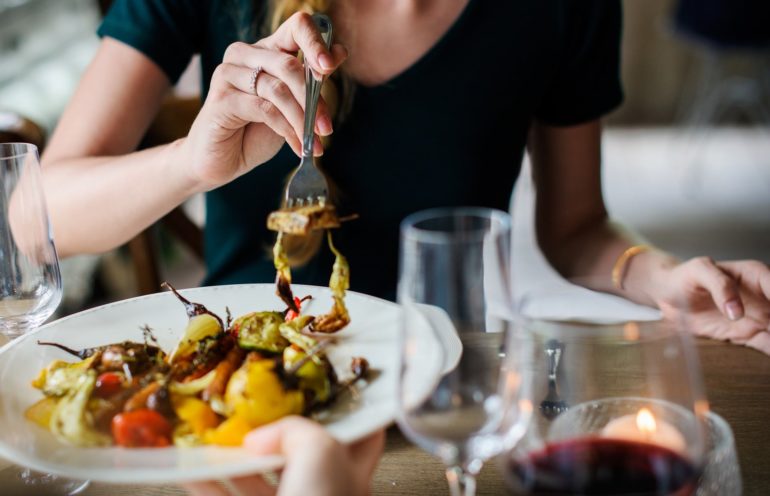 9 Restaurants To Take Your Family To In Columbus That Aren't Chain Restaurants 9 Person dining on grilled vegetables and meat using fork at restaurant table with glasses.