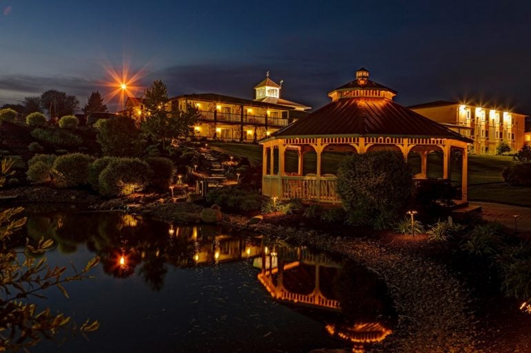 Illuminated red-roofed gazebo and resort buildings reflected in a pond at twilight