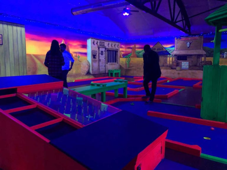 Show Off Your Perfect Putt Putt Skills at Miner49er Mini-Golf 2 Colorful indoor mini golf course with neon lighting and Western-themed backdrop at Miner 49er