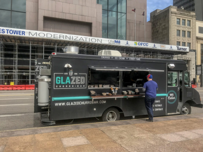 Black food truck with "Glazed" branding serves churros and ice cream on urban street.