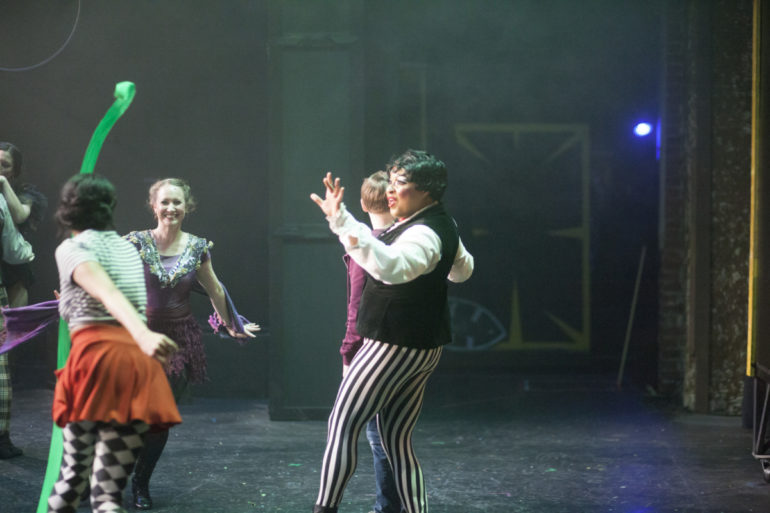 Costumed performers in motion on a hazy green-lit stage during a production