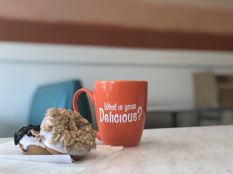 Red mug with "What is your Delicious?" text next to a s'mores dessert on table.