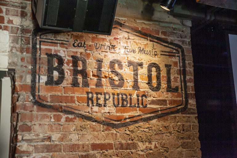 Weathered brick wall sign reading "Eat Drink Live Music" with "Brassy" and "Republic" text visible.