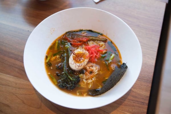 Bowl of ramen with broth, noodles, egg, vegetables, and garnish on wooden table.