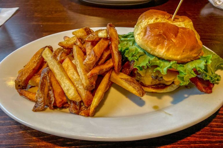 Burger with lettuce and bacon on a toasted bun with a side of fries