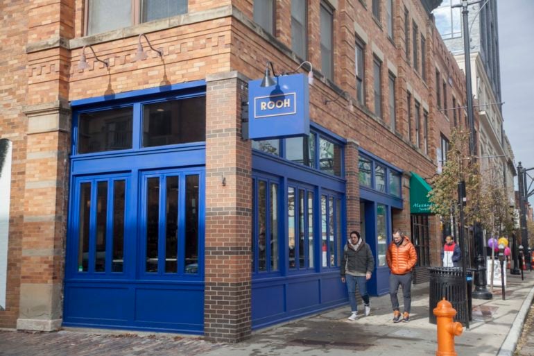Bright blue storefront with ROOH sign on brick corner building with pedestrians outside.