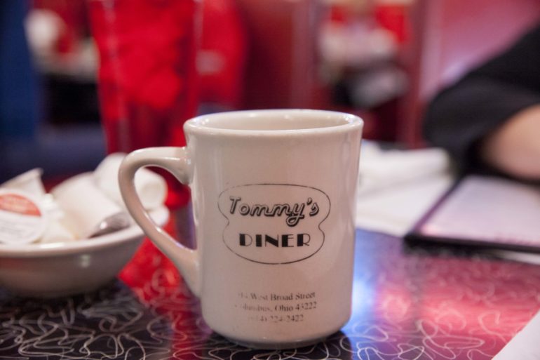Tommy's Diner In Franklinton Is A Columbus Classic 4 White ceramic mug from Tommy's Diner sits on a table with red holiday decorations in background.