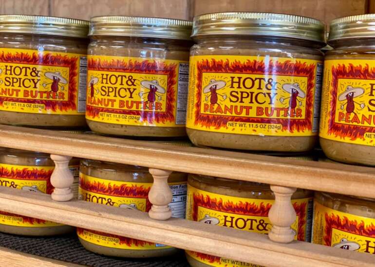 Stop What You're Doing And Get Yourself To Krema Nut Company 3 Jars of Krema Nut Company's Hot & Spicy Peanut Butter on a wooden shelf
