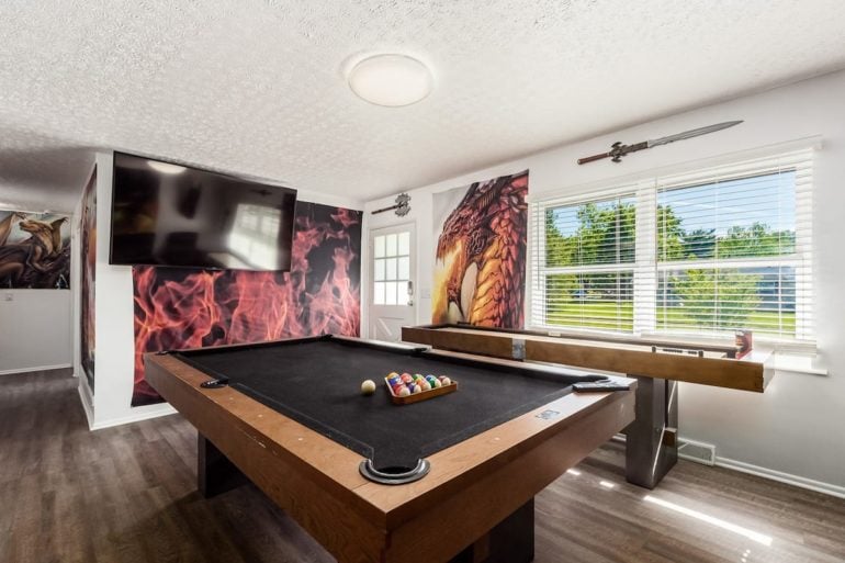 This Dragon-Themed Airbnb In Westerville Has Its Own Mini Golf Course 3 Modern recreation room with pool table, mounted TV, and large windows overlooking green landscape.