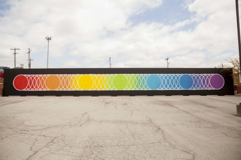 A colorful rainbow mural with concentric circles on a black wall in an urban plaza.