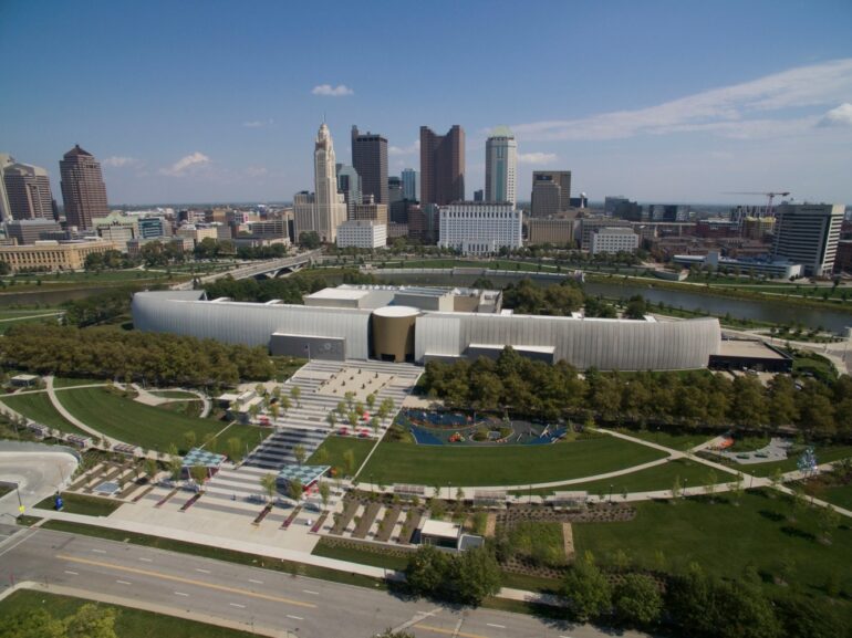 COSI Is Hosting A Magical, Adults-Only Yule Ball This December 10 Aerial view of COSI science center with the downtown Columbus skyline behind it