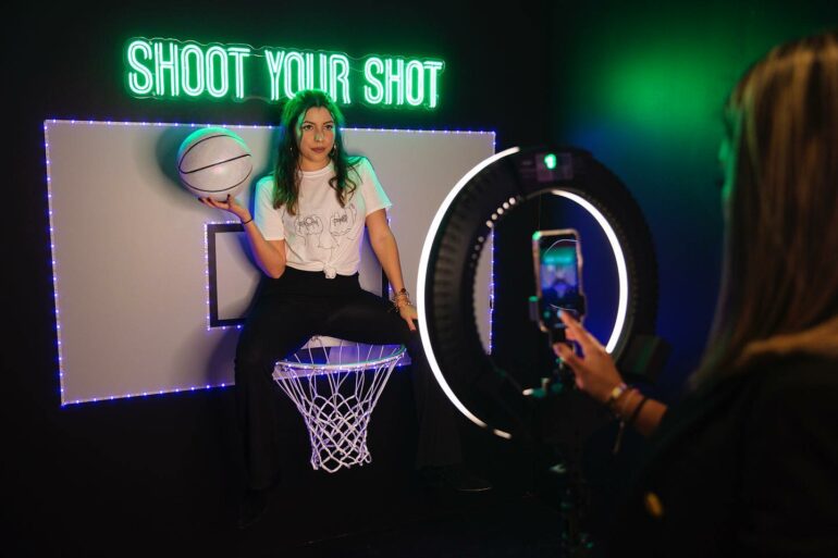 This Colorful Selfie Museum Is Coming To Columbus 1 Woman posing with basketball at neon-lit interactive game installation for photo.
