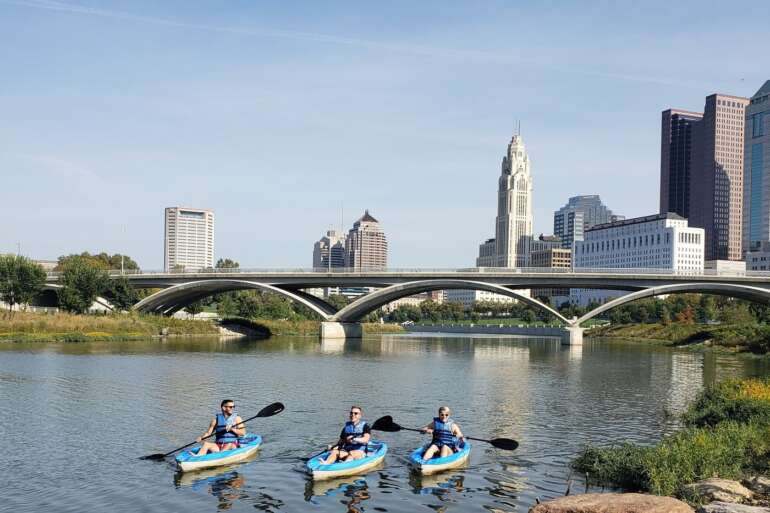 These Beautiful Kayaking Routes Will Make You Drop What You're Doing And Head Straight For The Water 2 Kayakers paddling the Scioto River with the downtown Columbus skyline behind them