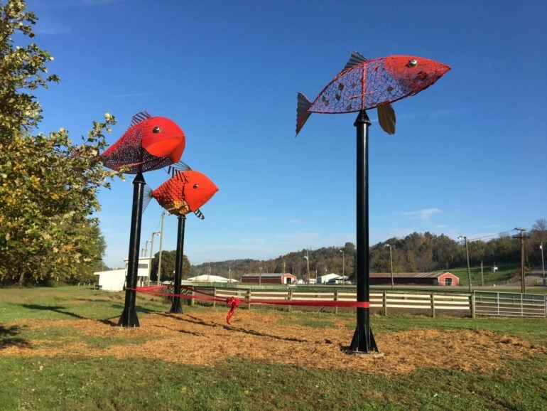 The Ohio Art Corridor Is A 132-Mile Road Trip Full Of Fantastic Public Art 10 Colorful red fish sculptures mounted on black poles in a rural park setting.