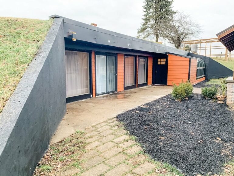 This Underground Earth Home In Hocking Hills Is A One-Of-A-Kind Getaway 3 Earth-sheltered home exterior with orange siding, black trim, and grassy roof