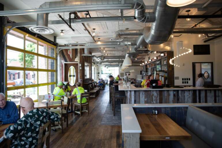 Tee Jaye's Kitchen + Spirits Has Modern Farmhouse Vibes And A Delicious Menu 7 Modern industrial-style restaurant interior with counter seating, exposed ductwork, and large storefront windows.