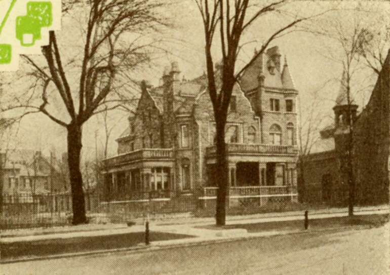 Historic Victorian mansion with tower surrounded by bare trees and iron fence.