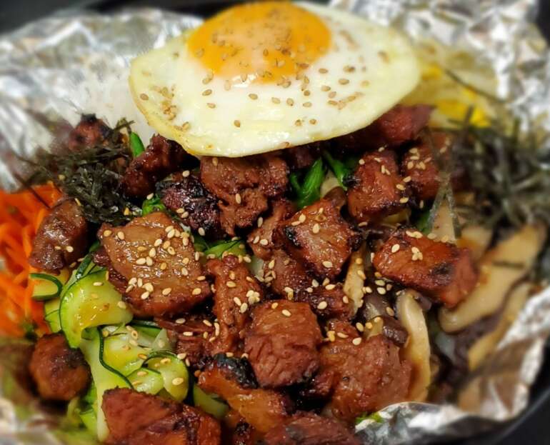 Grilled beef topped with a fried egg, sesame, and vegetables at Gogi Korean BBQ