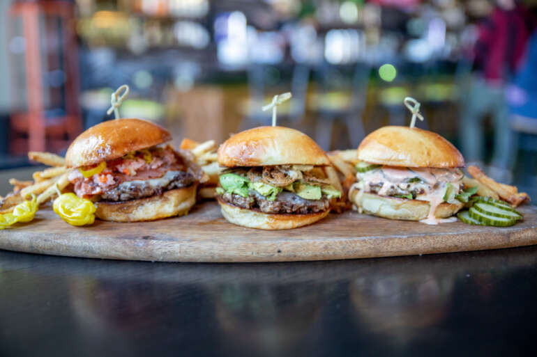 A Burger From Butcher's Galley Will Be The Best Thing You Eat This Week 2 Three gourmet burgers on a wooden board with fries and garnishes