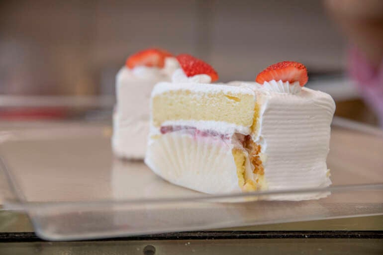Sliced strawberry cake with whipped cream frosting and fresh strawberry garnish from Golden Delight Bakery