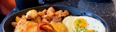 A cast iron skillet serves breakfast with eggs, bacon, hash browns, and melted cheese.