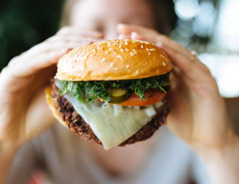 The Best Veggie Burgers In Columbus 3 Person holds a veggie burger topped with cheese, kale, tomato, and pickle at Northstar Cafe