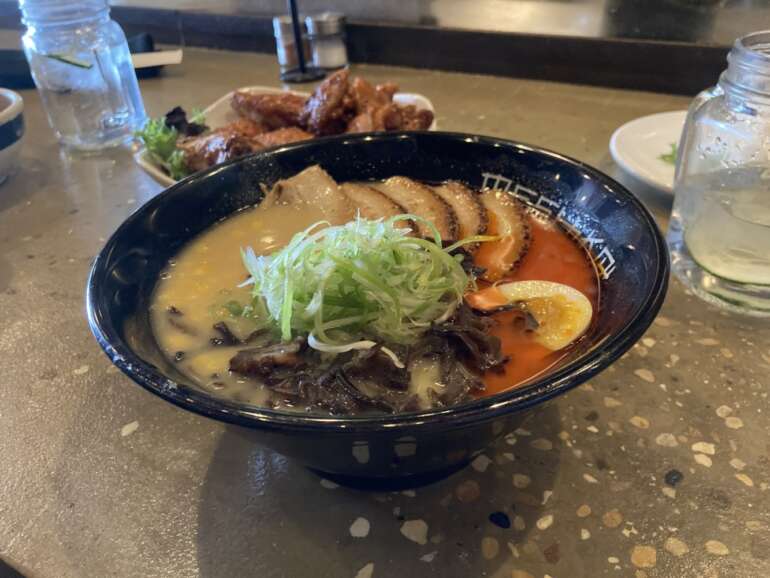 Bowl of ramen with broth, noodles, egg, and green onions garnish at restaurant.