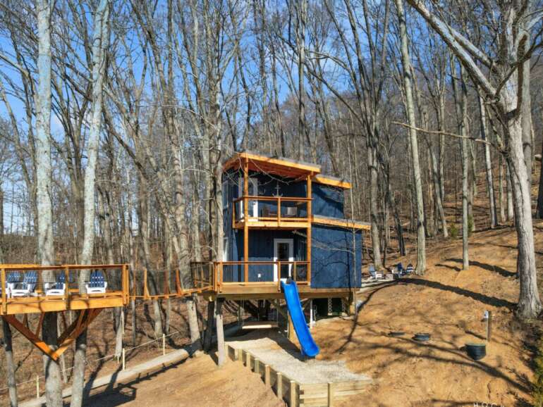 This Luxury, Lakefront Treehouse In Hocking Hills Has All The Amenities, Including A Private Concierge 4 Modern treehouse with orange wood frame and blue slide nestled among bare trees.