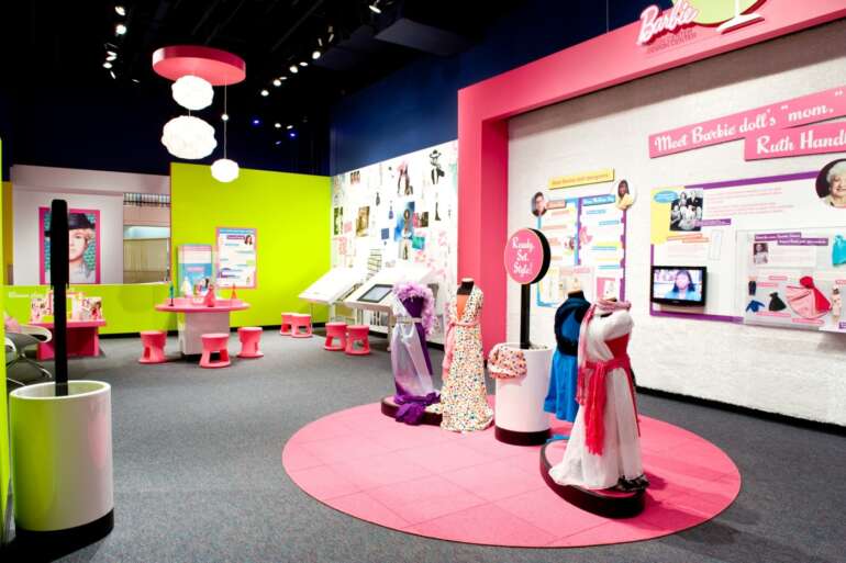 Barbie Is Coming To COSI 9 Colorful Barbie-themed exhibition space with pink and lime green walls, mannequins, and interactive displays.