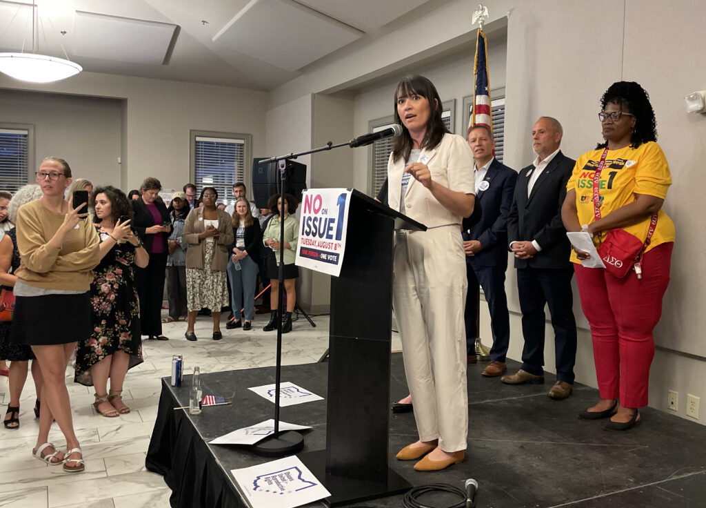 Ohio’s Issue 1 Goes Down To Defeat 1 Woman speaking at a podium with a No on Issue 1 sign surrounded by supporters
