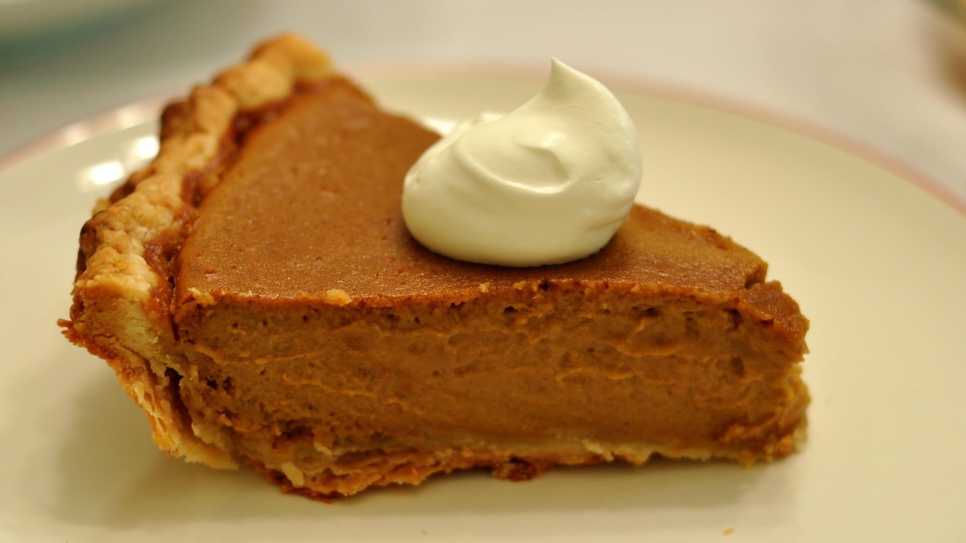 Slice of pumpkin pie topped with whipped cream on a plate
