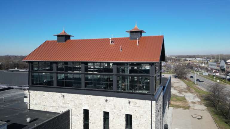 A Massive Distillery Expansion Unveiled by Middle West Spirits in East Columbus 3 Modern multi-story building with red metal roof and two cupolas overlooking suburban street.