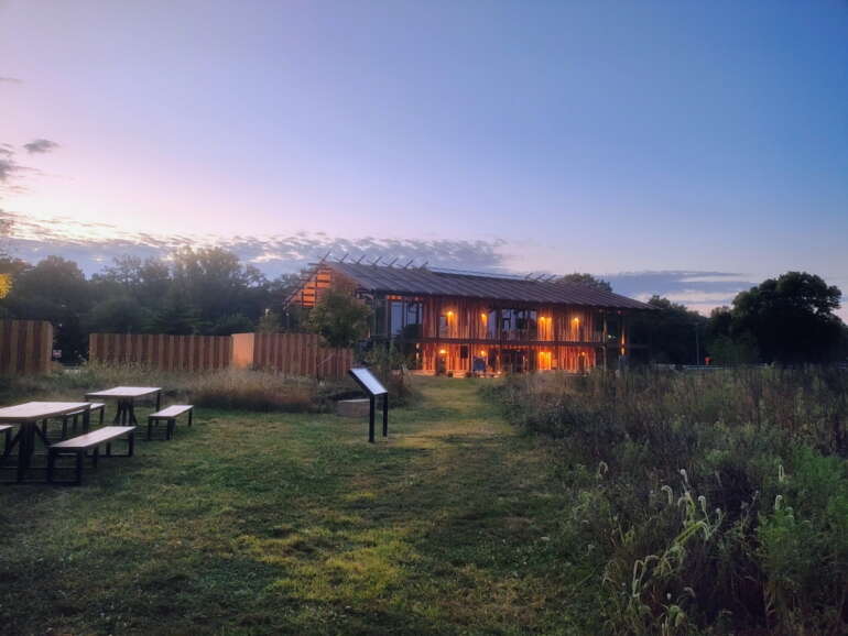 History Meets Nature at Ohio’s Great Council State Park 3 Modern barn lit warmly at dusk with picnic tables and native plantings in foreground during twilight hour.